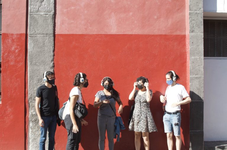 Personas con auriculares frente a un muro rojo.